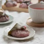 桜もちが白いお皿に一つ入っている。近くにお茶が添えられている。